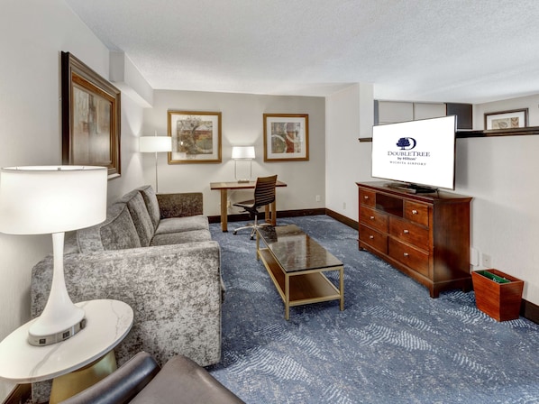 Une chambre d’hôtel équipée d’un canapé, d’un fauteuil, d’un bureau, d’une télévision et d’une petite armoire.