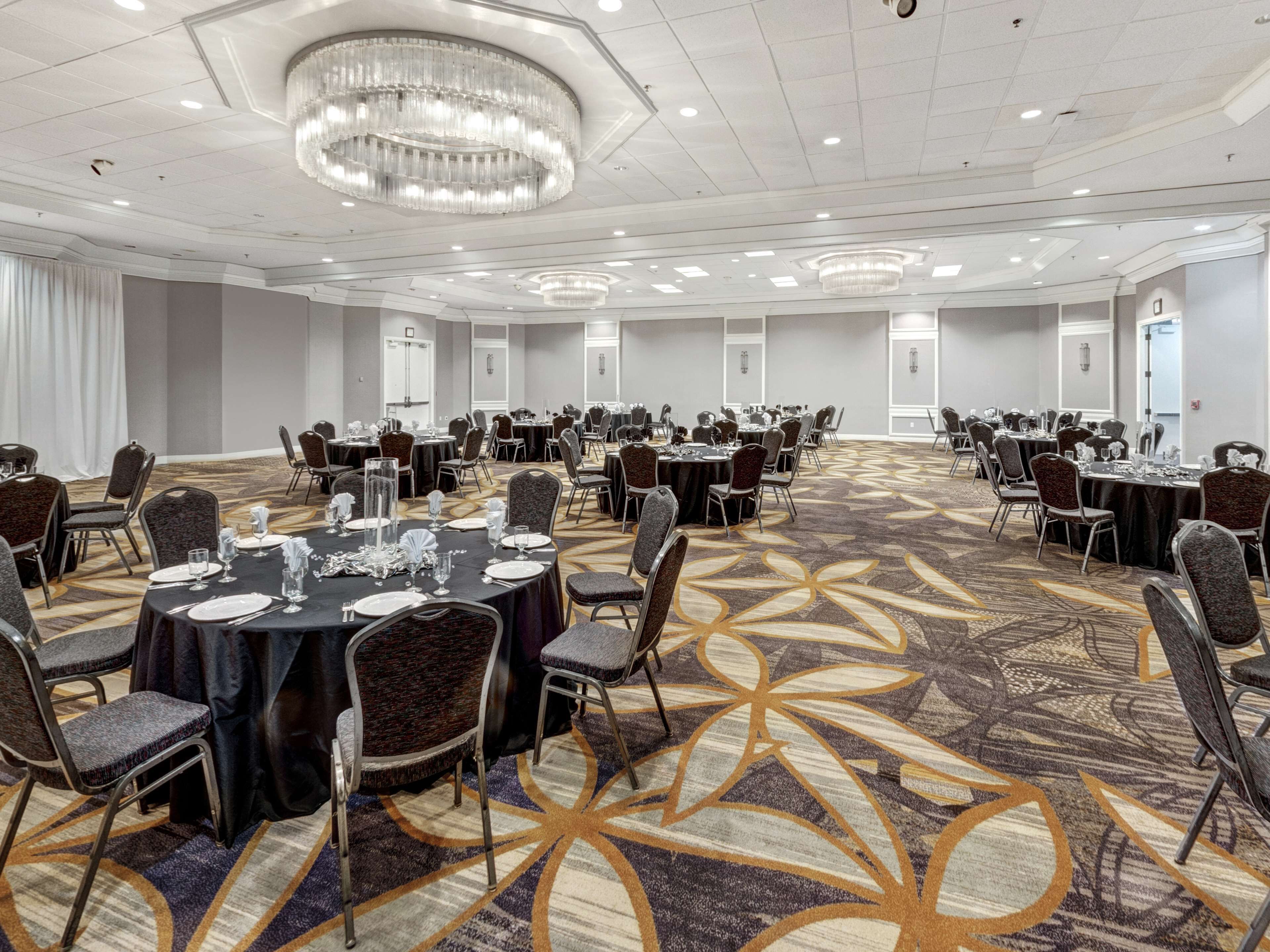 A large conference room with round tables and chairs, a patterned carpet, and a chandelier.