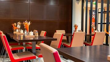 Un espace repas moderne avec une table en bois foncé, des chaises beiges et rouges, et des centres de table ornés de motifs floraux.
