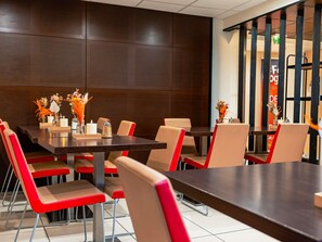 Un comedor moderno con una mesa de madera oscura, sillas beige y rojas, y centros de mesa con flores.