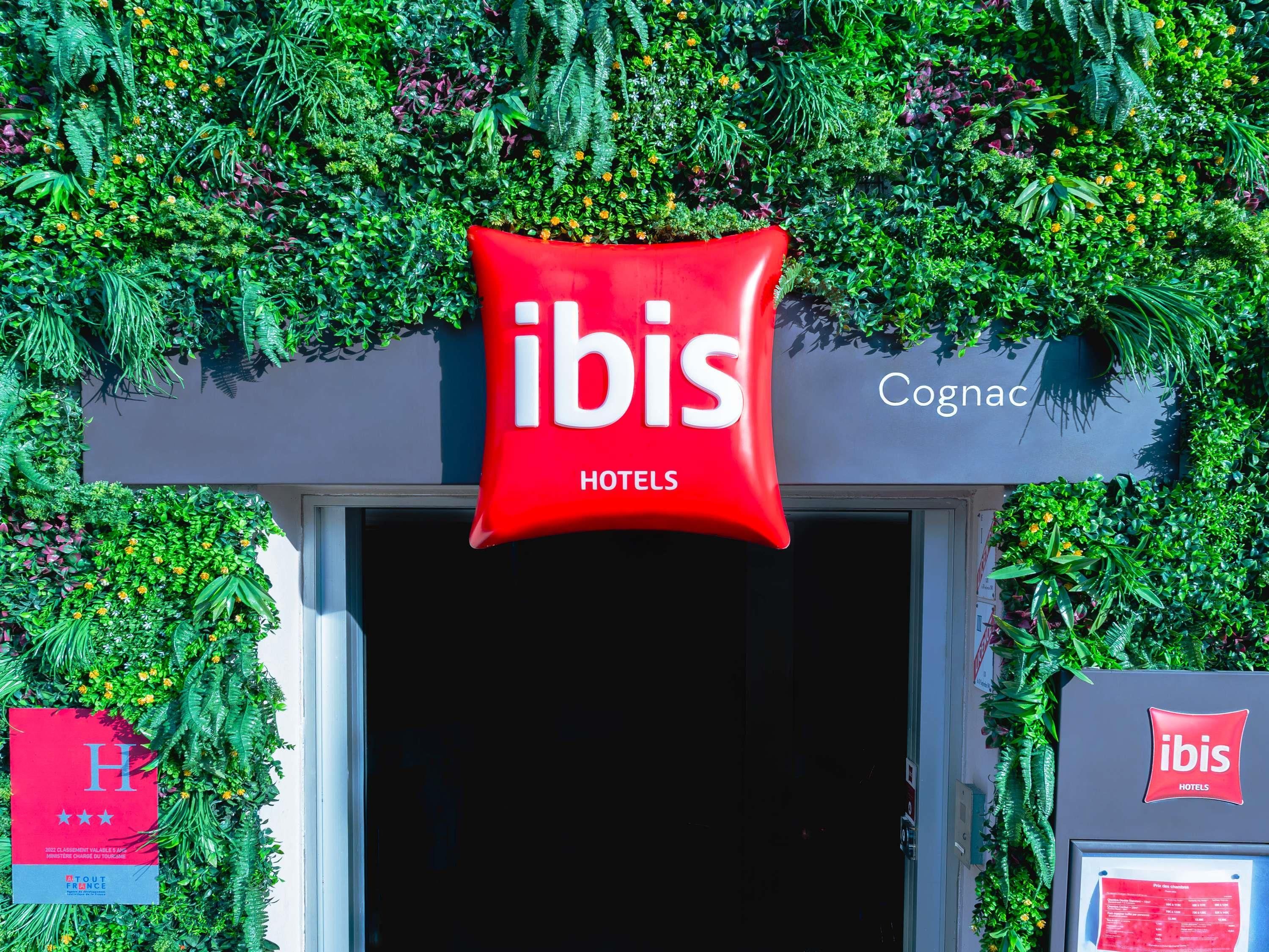 Entrada de un hotel con un cartel de 'ibis HOTELS', un cartel de 'Cognac' y un logotipo rojo de 'ibis'.