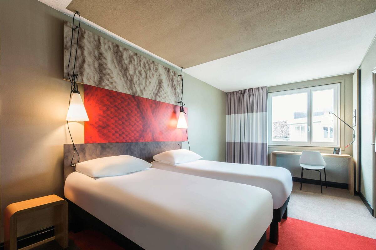 Une chambre d’hôtel avec deux lits, un bureau et une fenêtre avec des rideaux.