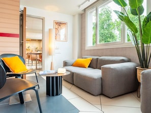 A modern living room with a sofa, a chair, a coffee table, and a large window with a view of greenery.