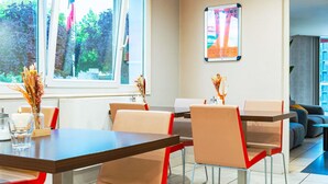 Un comedor moderno con mesas y sillas, un cartel en la pared y vistas al exterior con vegetación.