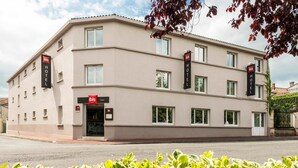 Een modern hotelgebouw met een platte gevel, meerdere ramen en een opvallend 'ibis' logo.