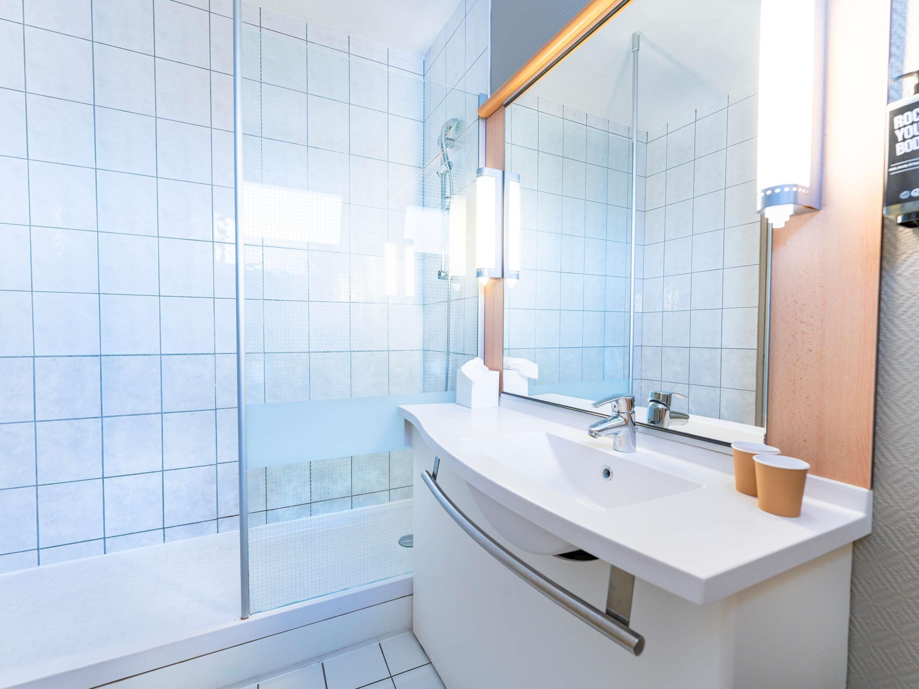 A modern bathroom with a glass shower enclosure, a white sink, and a large mirror.