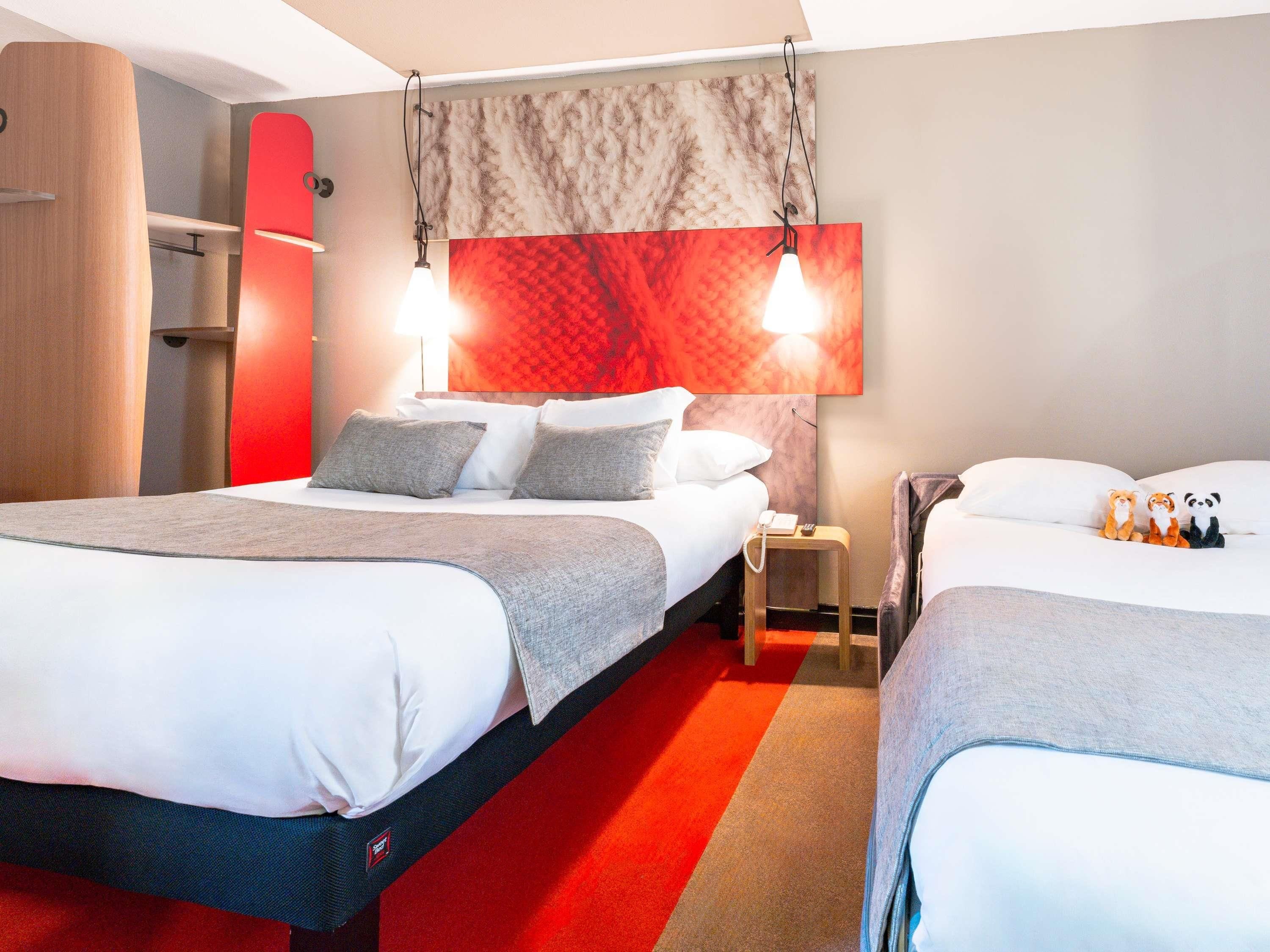 A hotel room with a large bed, a bedside table, a lamp, and a red carpet.