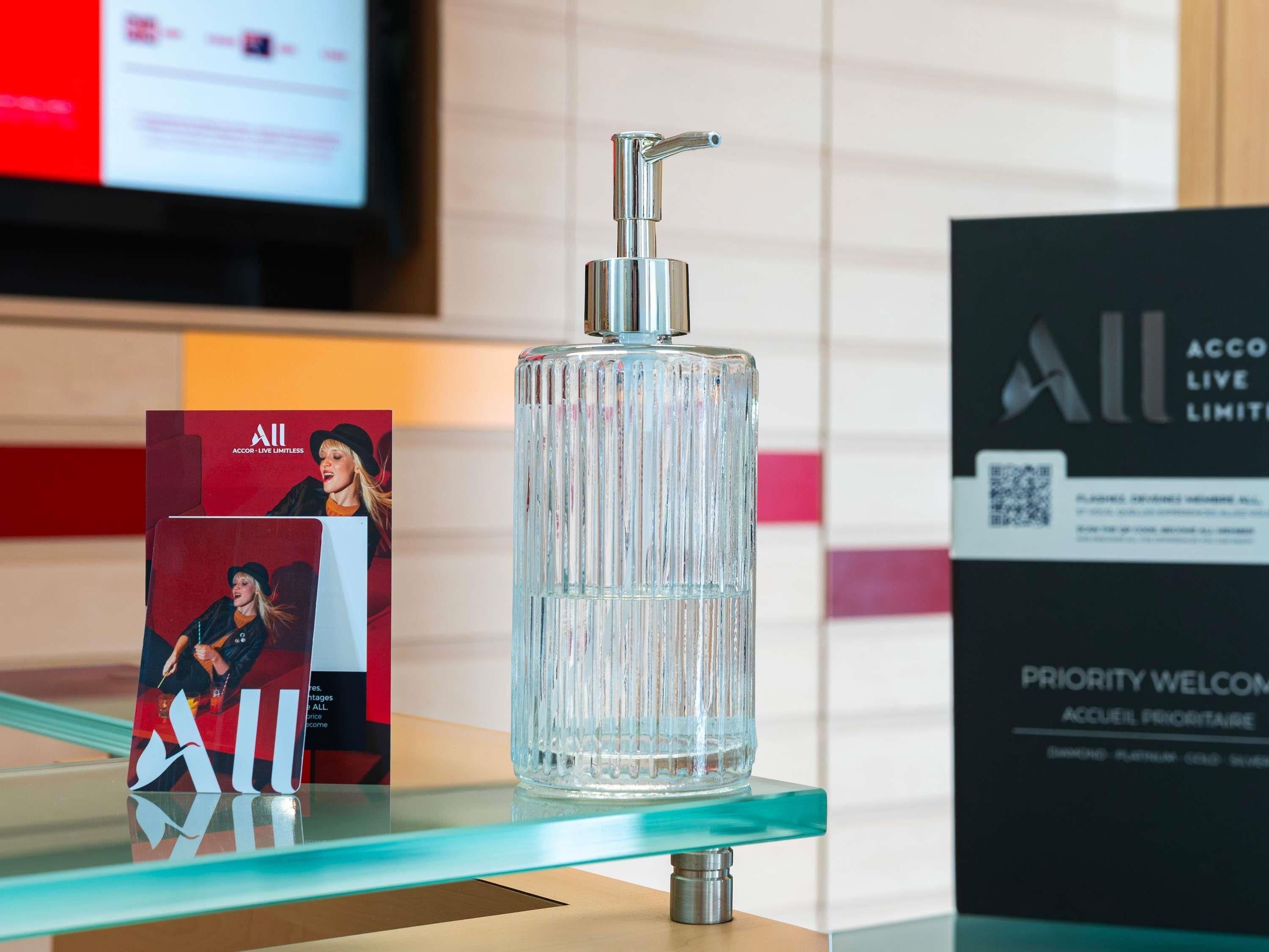 A clear glass bottle with a pump dispenser on a glass table, surrounded by promotional materials.