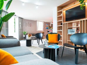 A modern living room with a sofa, chairs, a coffee table, and a TV on a wooden shelf. - ibis Cognac Centre (Cognac)