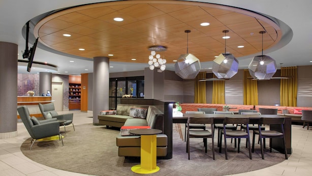 A modern hotel lobby with a curved ceiling, a seating area with sofas and chairs, a small dining table, and a reception desk. - SpringHill Suites Cincinnati North/Forest Park (Cincinnati)