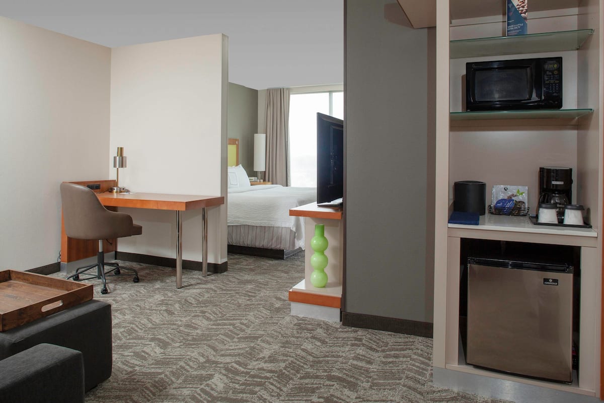 A hotel room with a bed, a desk with a chair, a television, a microwave, a coffee maker, and a mini-fridge.
