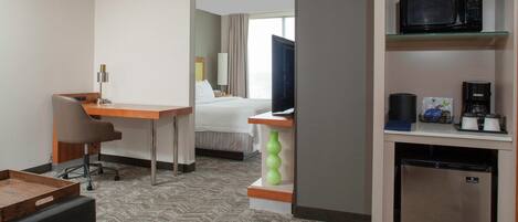 A hotel room with a bed, a desk with a chair, a television, a microwave, a coffee maker, and a mini-fridge.