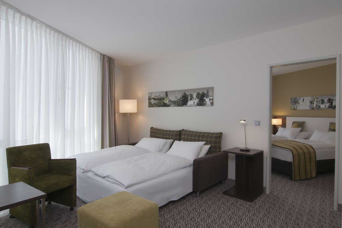 Una camera d'hotel con un letto, una sedia, un comodino, una lampada e un quadro appeso al muro.