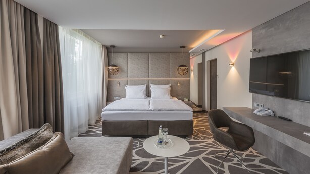 A modern hotel room with a large bed, a TV, a desk, and a sofa. - Holiday Inn Munich-Unterhaching by IHG (Unterhaching)