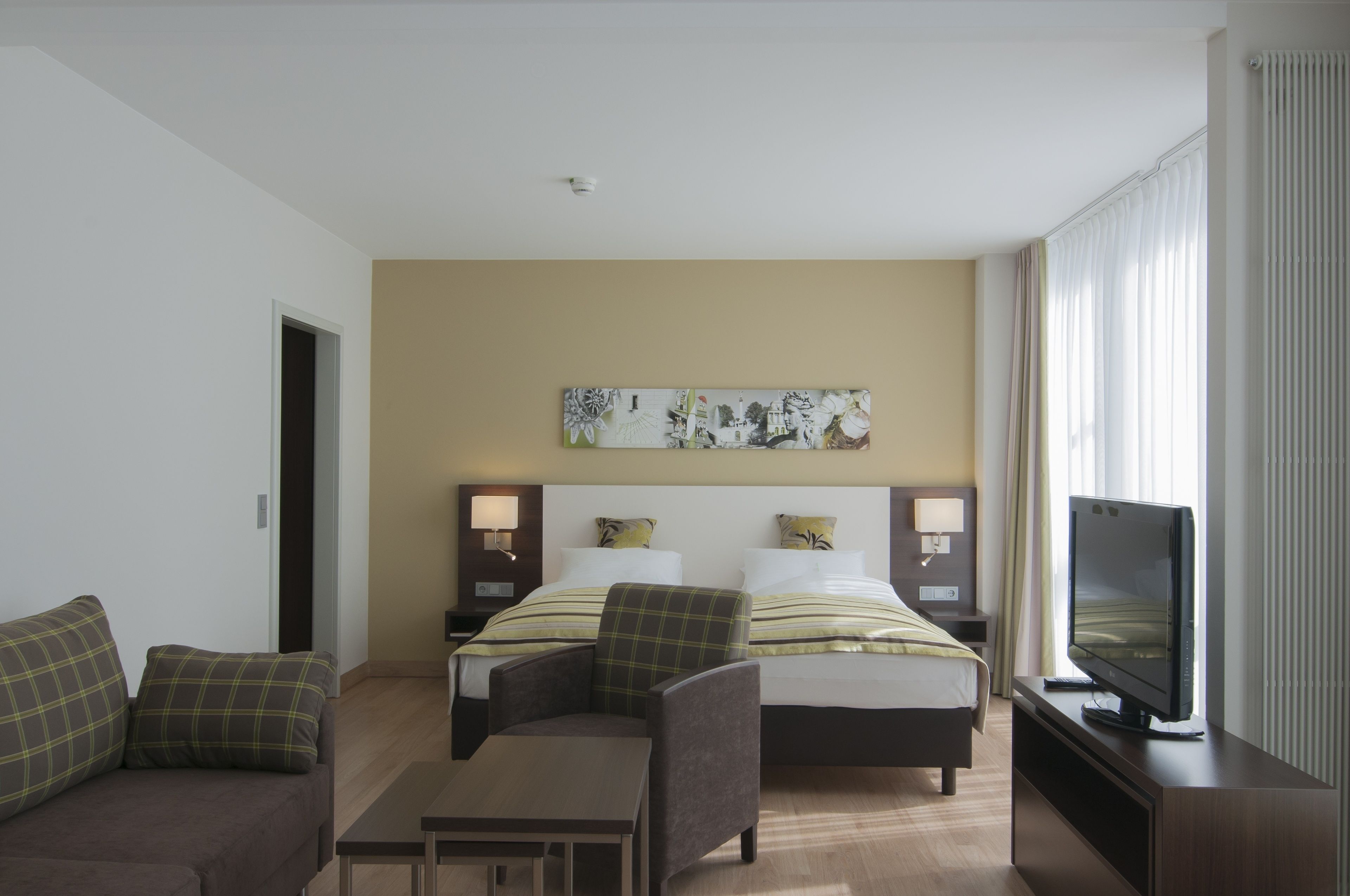 Une chambre d’hôtel avec un lit, deux tables de chevet, une télévision, un canapé et un tableau au mur.