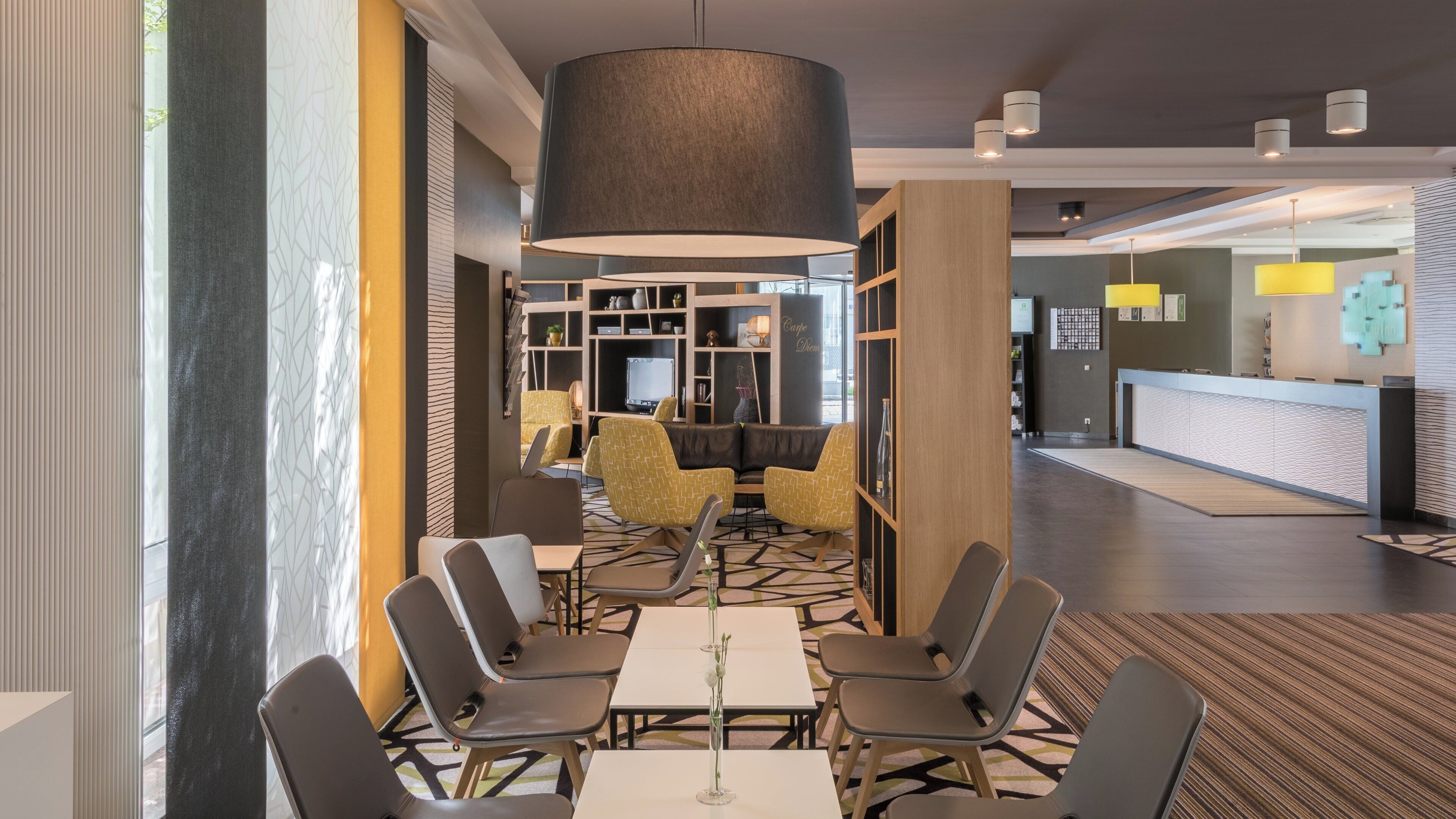 Eine moderne Hotelhalle mit einer Rezeption, einer Sitzecke und einer großen Pendelleuchte.