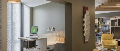 A modern office space with a desk, computer, and chair. There is a bookshelf with various items and a television in the background.