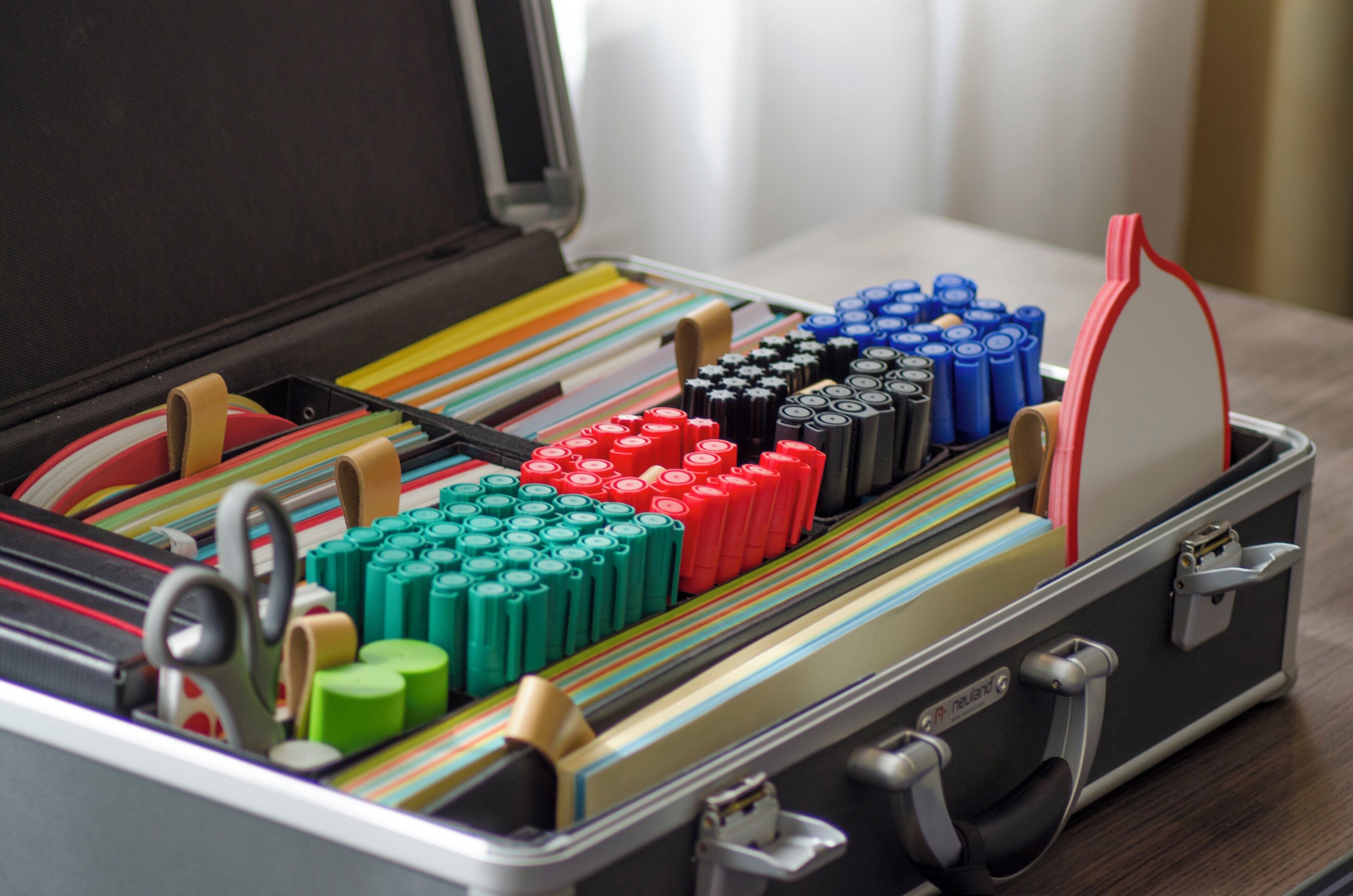 Une mallette avec des compartiments contenant divers articles de bureau, comme des stylos, des post-it et des piles.