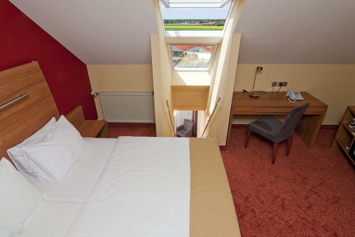 Une chambre d’hôtel équipée d’un lit, d’un bureau, d’une chaise, d’un radiateur et d’une lucarne.