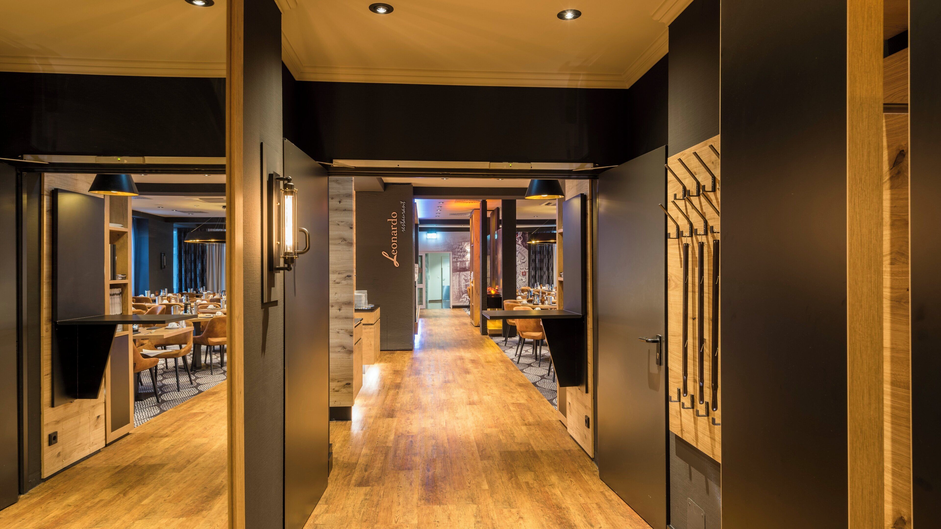 A hotel corridor with wooden flooring, a reception desk, and a dining area with tables and chairs.