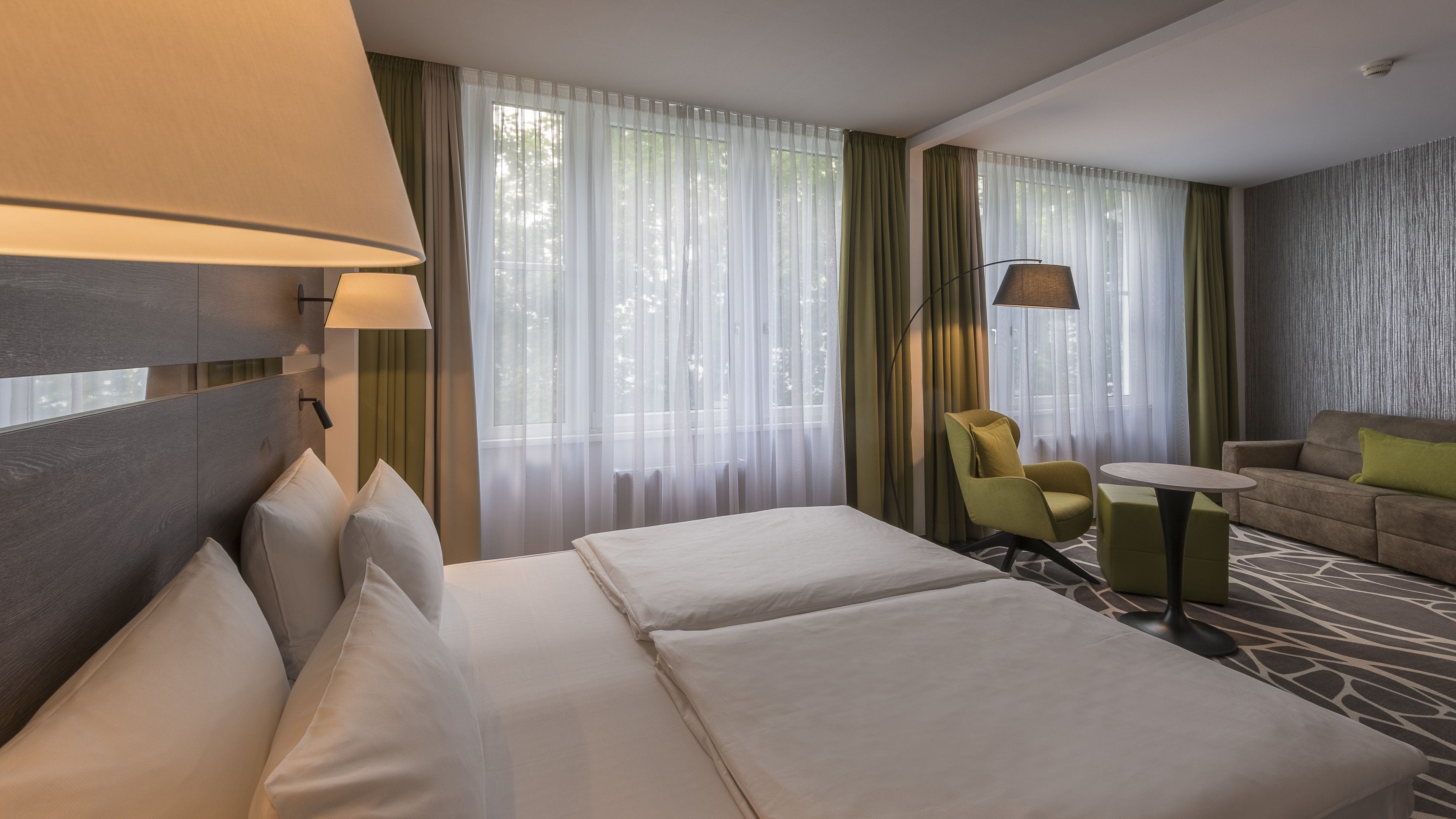 A hotel room with two beds, a sofa, a chair, a small table, and a lamp.