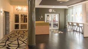 A hotel lobby with a reception desk, a seating area with bar stools, and a patterned carpet. - Holiday Inn Munich-Unterhaching by IHG (Unterhaching)