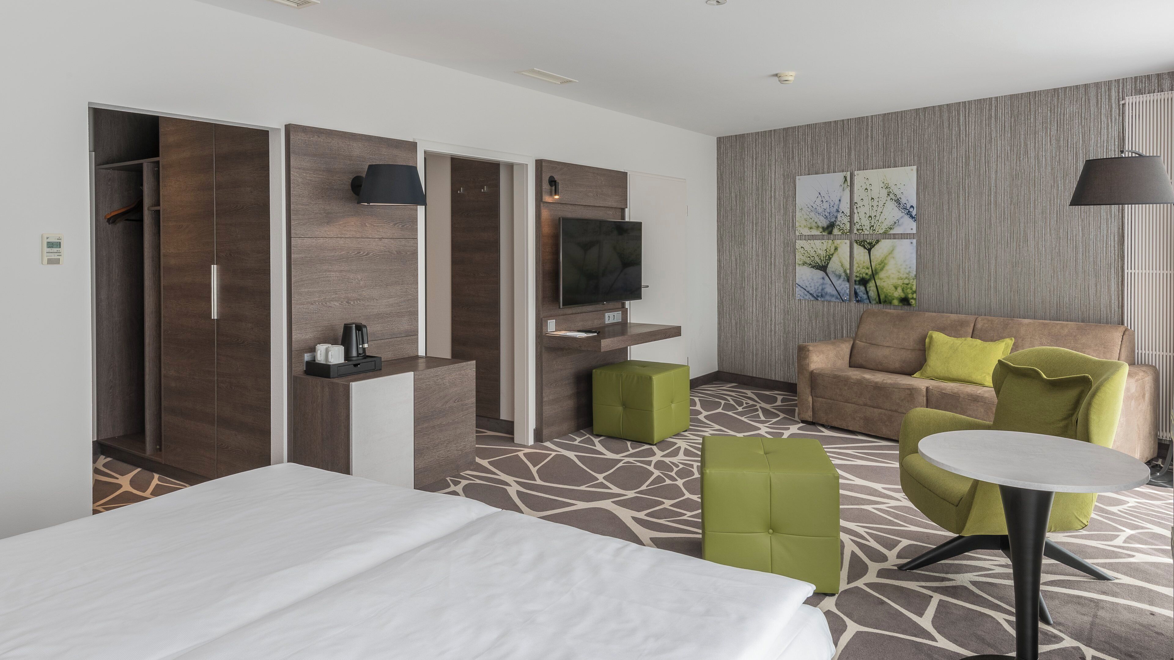 Een hotelkamer met een bed, een bank, een televisie, een koffieapparaat en een klein tafeltje.