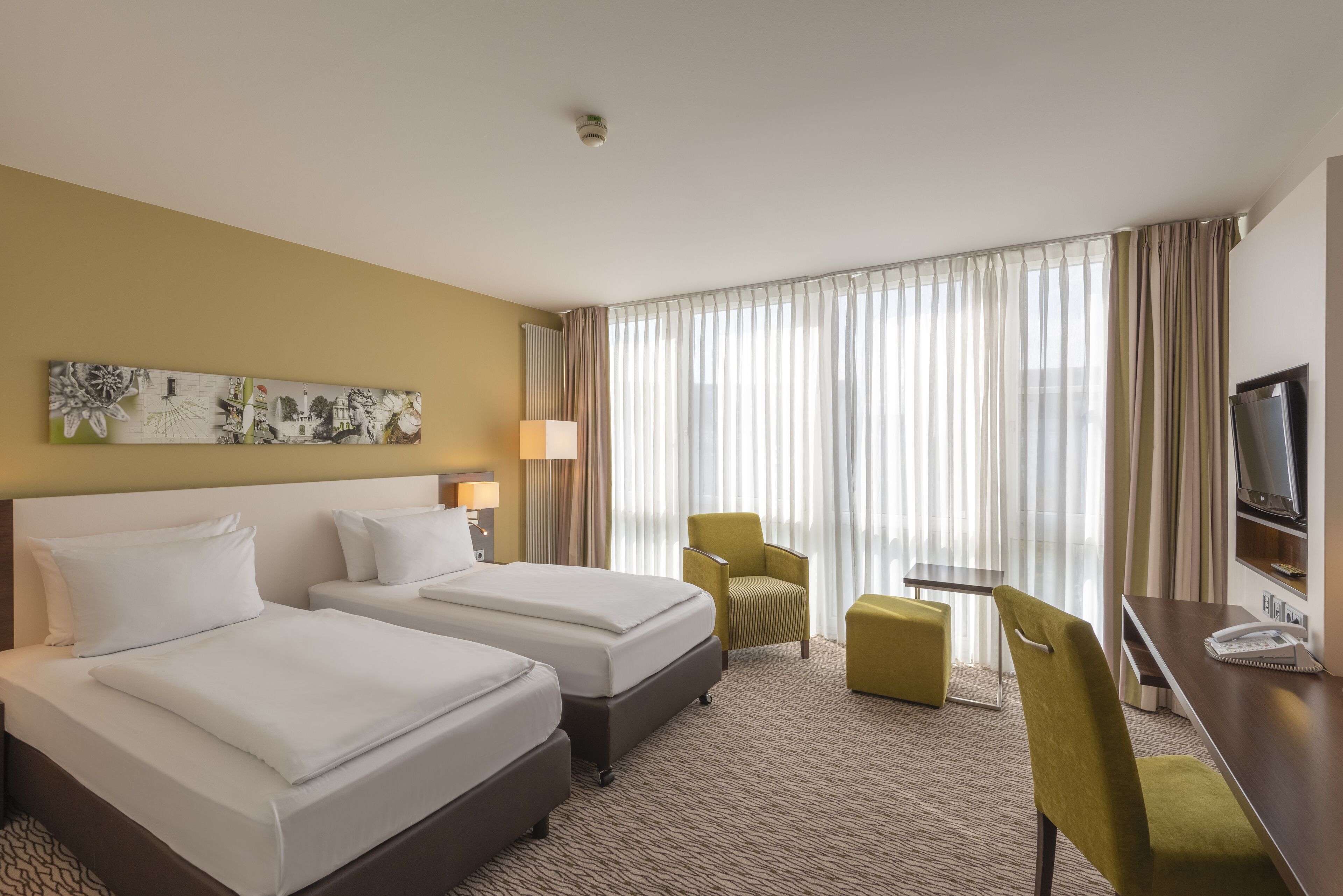 Une chambre d’hôtel avec deux lits, un bureau, une chaise, une télévision et une grande fenêtre avec des rideaux.