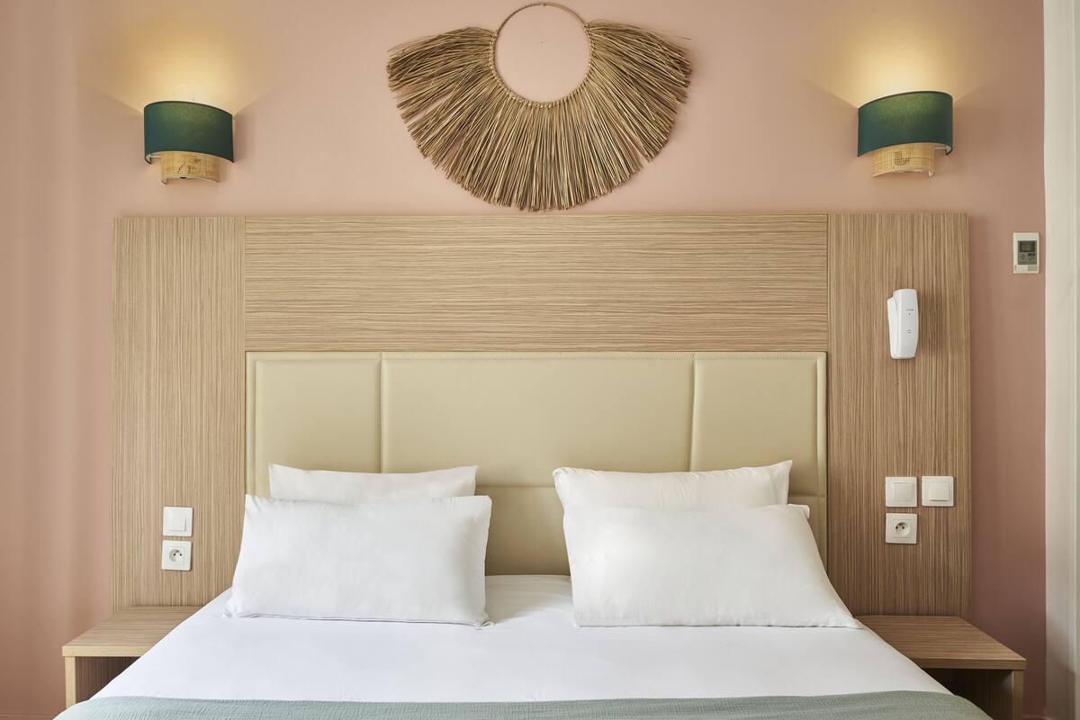 A hotel room with a large bed, two bedside tables, a wall-mounted light fixture, and a wall-mounted telephone.
