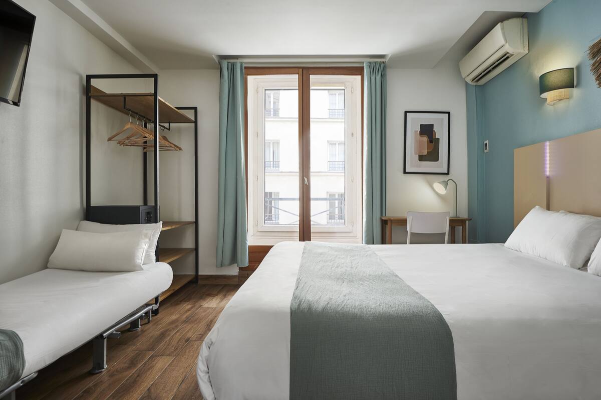 A hotel room with a bed, a desk, a chair, a wardrobe, and a window with curtains.
