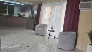 A spacious room with a tiled floor, two grey armchairs, a small round table, and a potted plant.