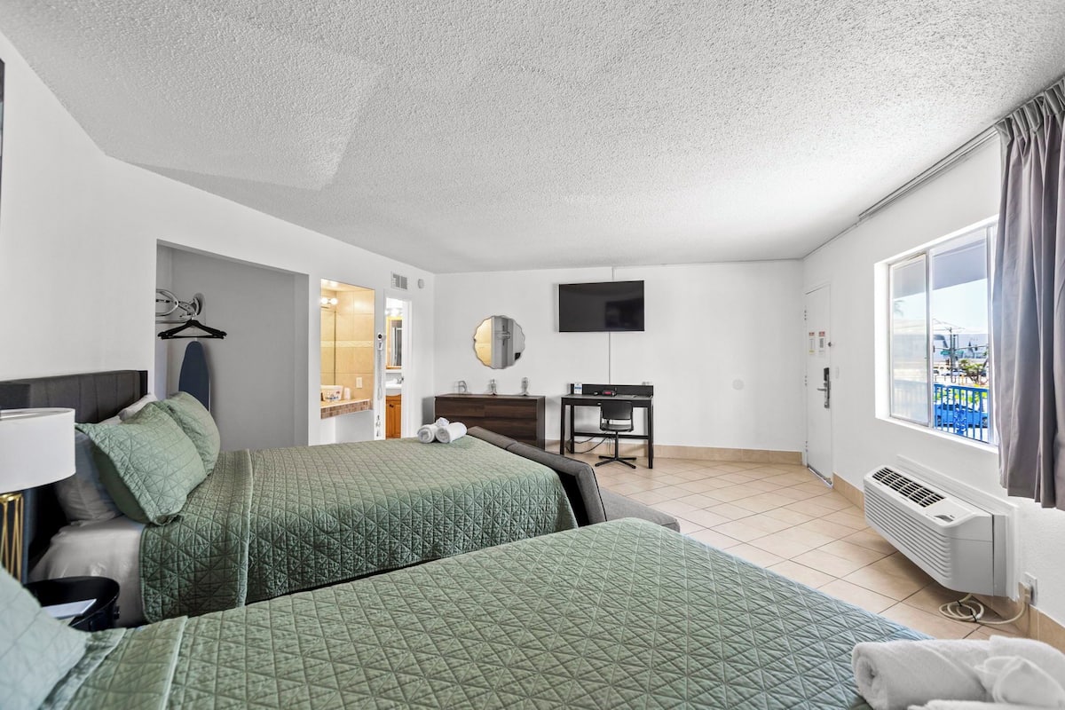 A hotel room with two beds, a desk, a TV, and a window with a view.