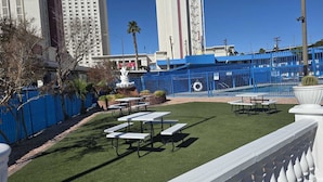 An outdoor patio area with tables and chairs, a pool, and a blue fence.