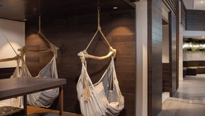 A modern interior with two hanging hammocks, a wooden table, and two leather chairs. - Cassia Hotel Jerusalem (Jerusalem)
