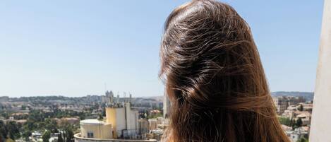 A person standing on a balcony overlooking a cityscape with buildings and a pool area.