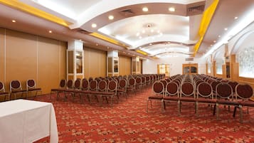 A conference room with rows of chairs, a white table, and a red carpeted floor.