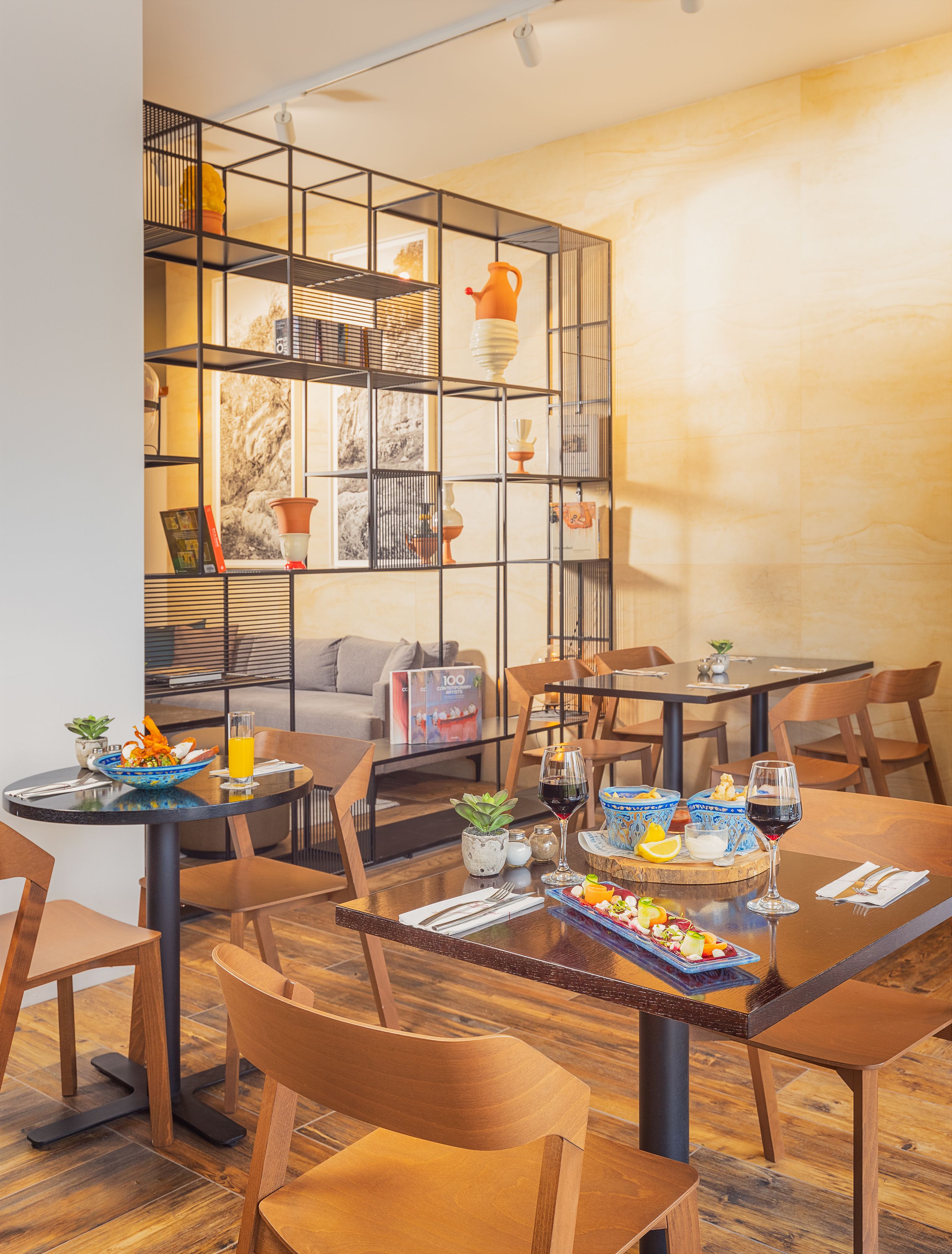 Uma sala de jantar moderna com mobiliário de madeira, uma mesa central com um copo de vinho tinto e uma estante decorativa ao fundo.