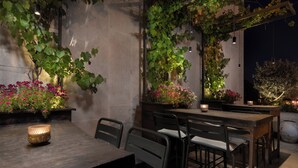 An outdoor dining area with a wooden table and chairs, surrounded by greenery and flowering plants. - Cassia Hotel Jerusalem (Jerusalem)