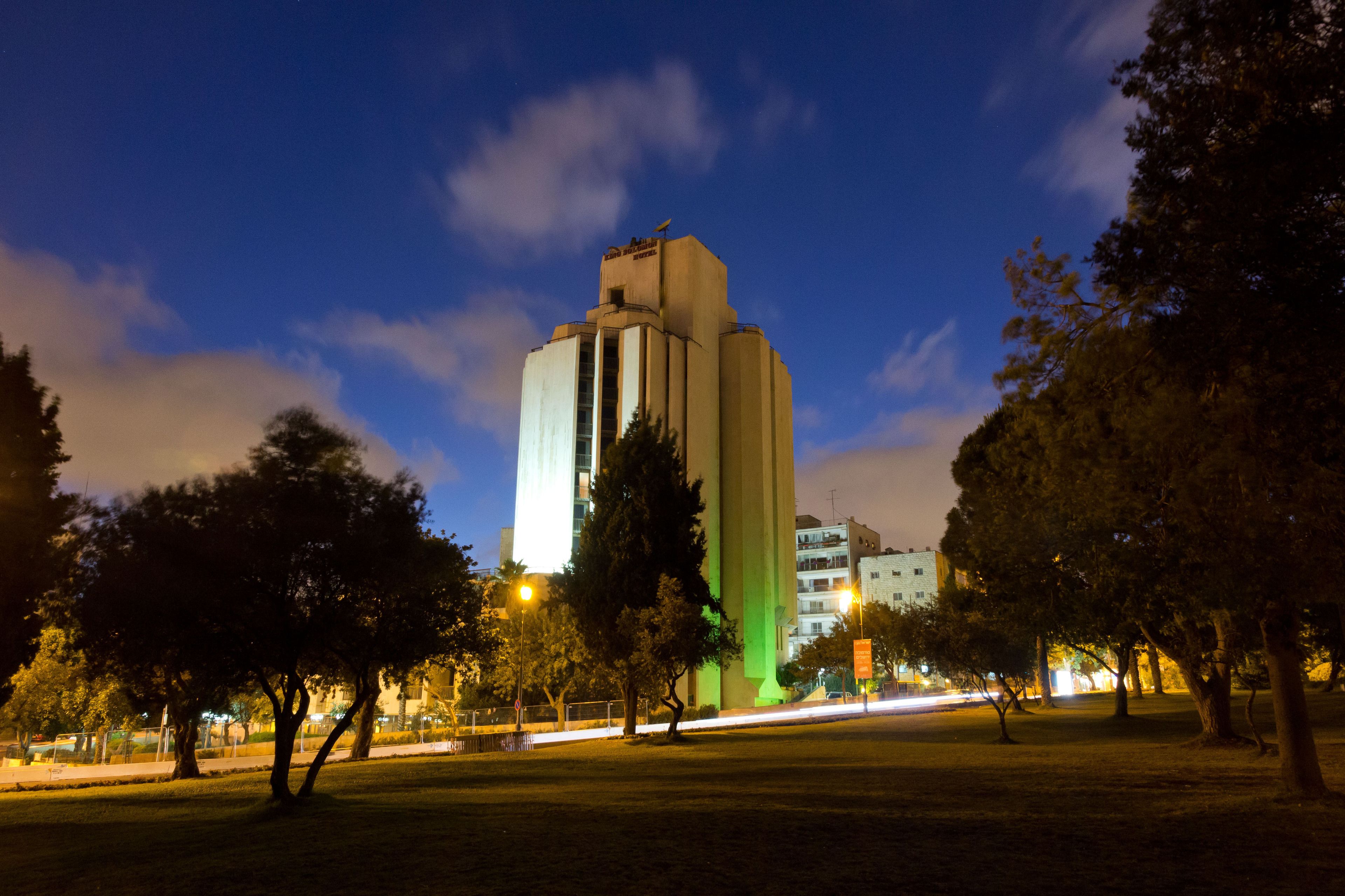 Un edificio alto y moderno con un diseño único, rodeado de árboles e iluminado por farolas.