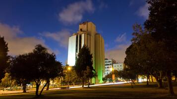 Un edificio alto y moderno con un diseño único, rodeado de árboles e iluminado por farolas.
