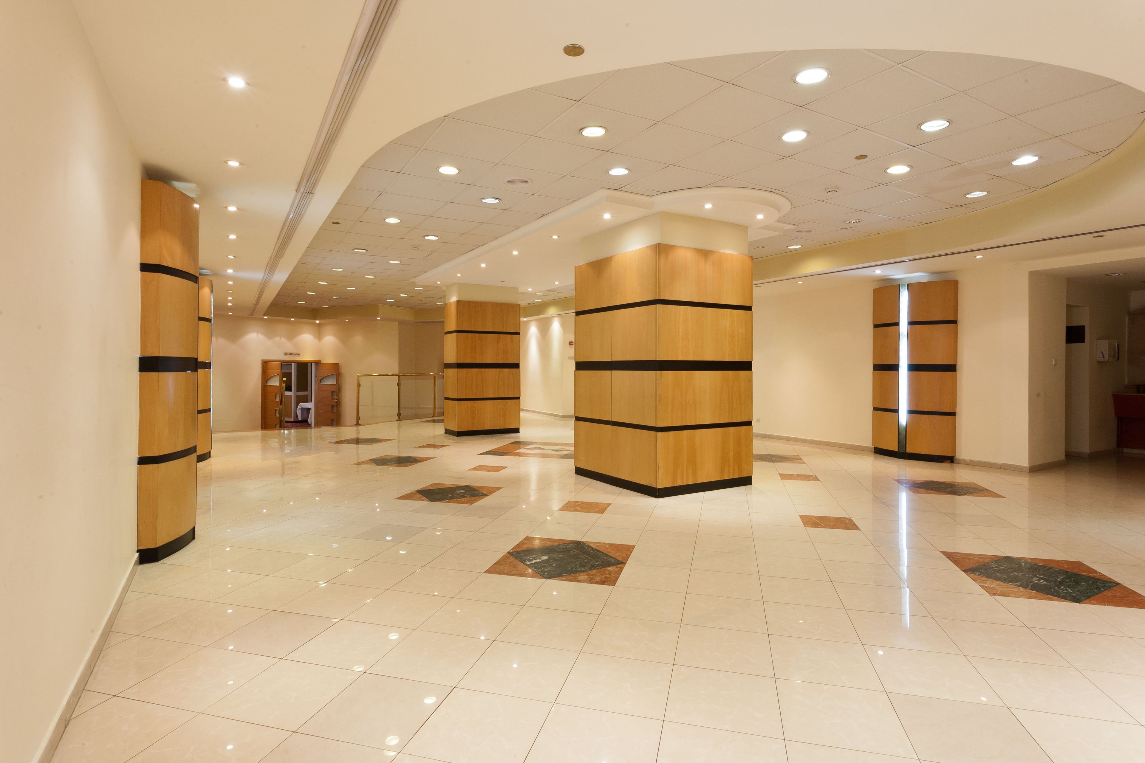 A spacious lobby with a polished tile floor, wooden pillars, and recessed ceiling lighting.