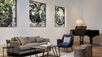 A modern living room with a sofa, armchair, coffee table, and a grand piano.