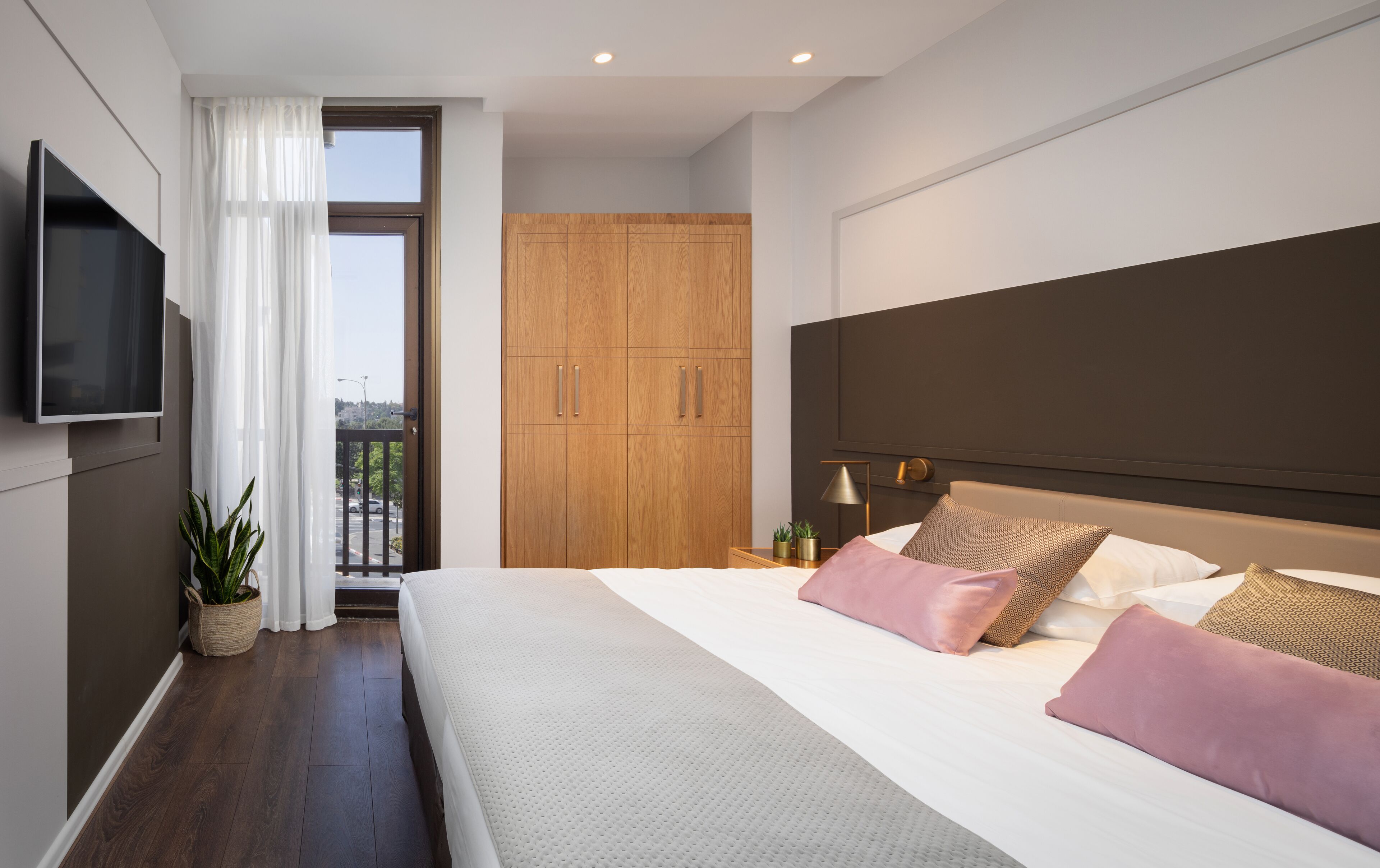 A modern bedroom with a large bed, a TV mounted on the wall, and a wooden wardrobe.
