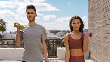 Two people exercising with dumbbells on a rooftop with a city view.