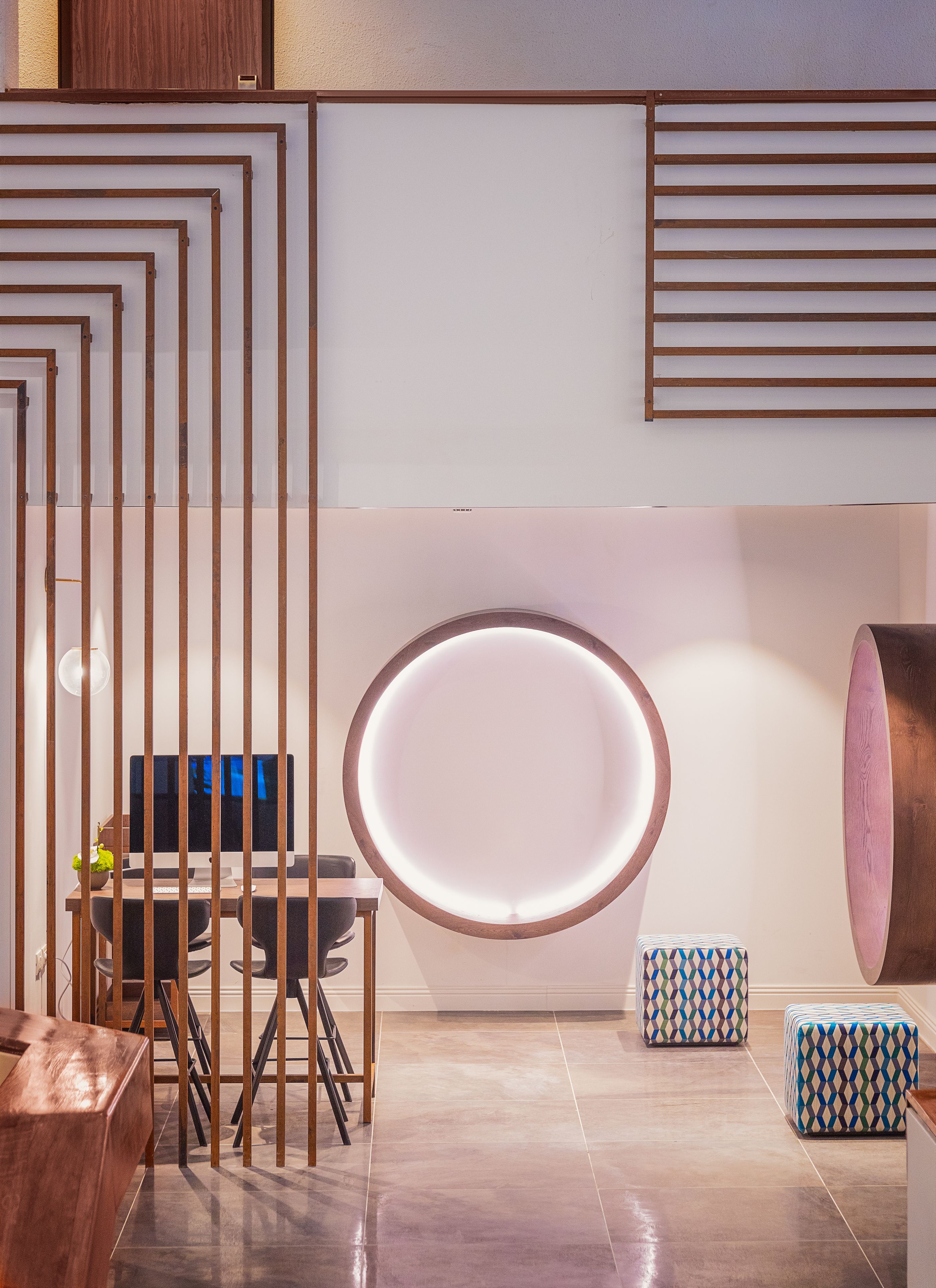 Una habitación moderna con un espejo grande, separadores de madera, un escritorio con computadora y otomanas estampadas.