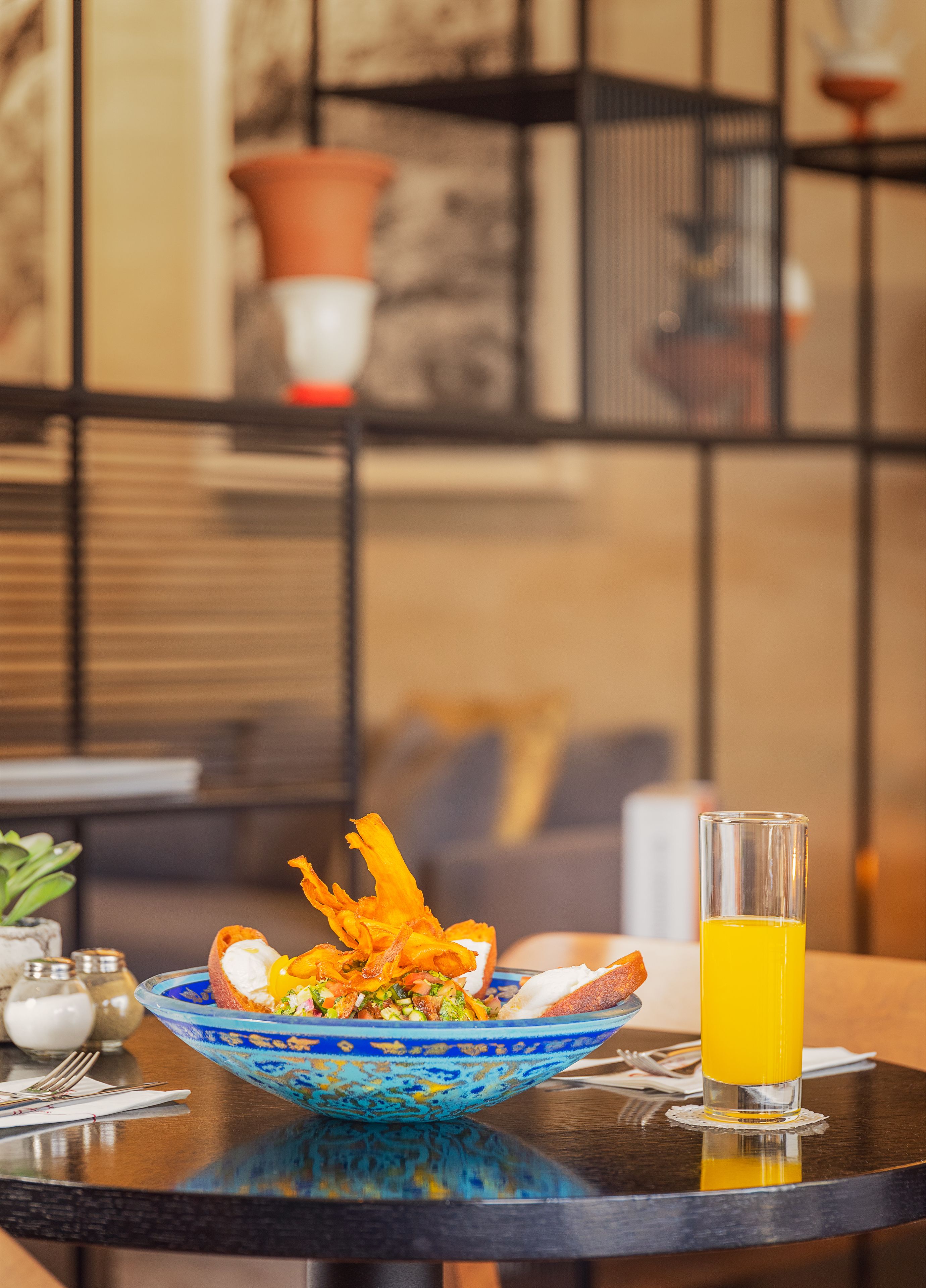 A dining table with a blue ceramic bowl containing a salad, a glass of orange juice, and a plate with bread and a white item.