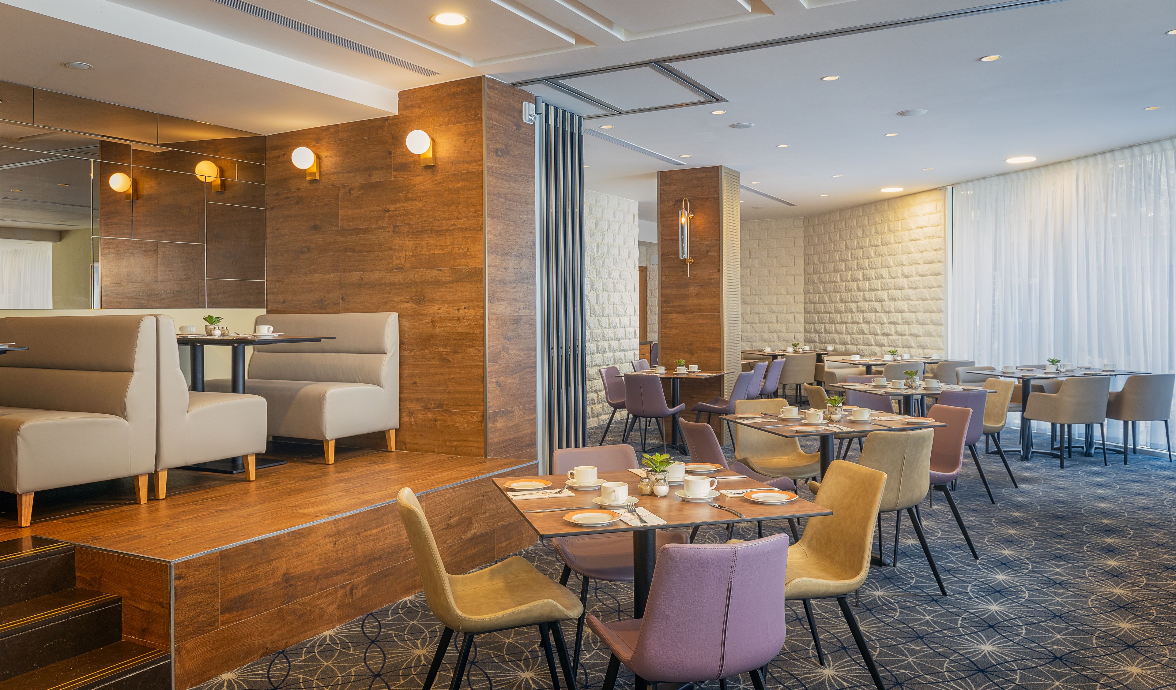 A modern dining area with high tables and cushioned chairs, wooden accents, and a patterned carpet.