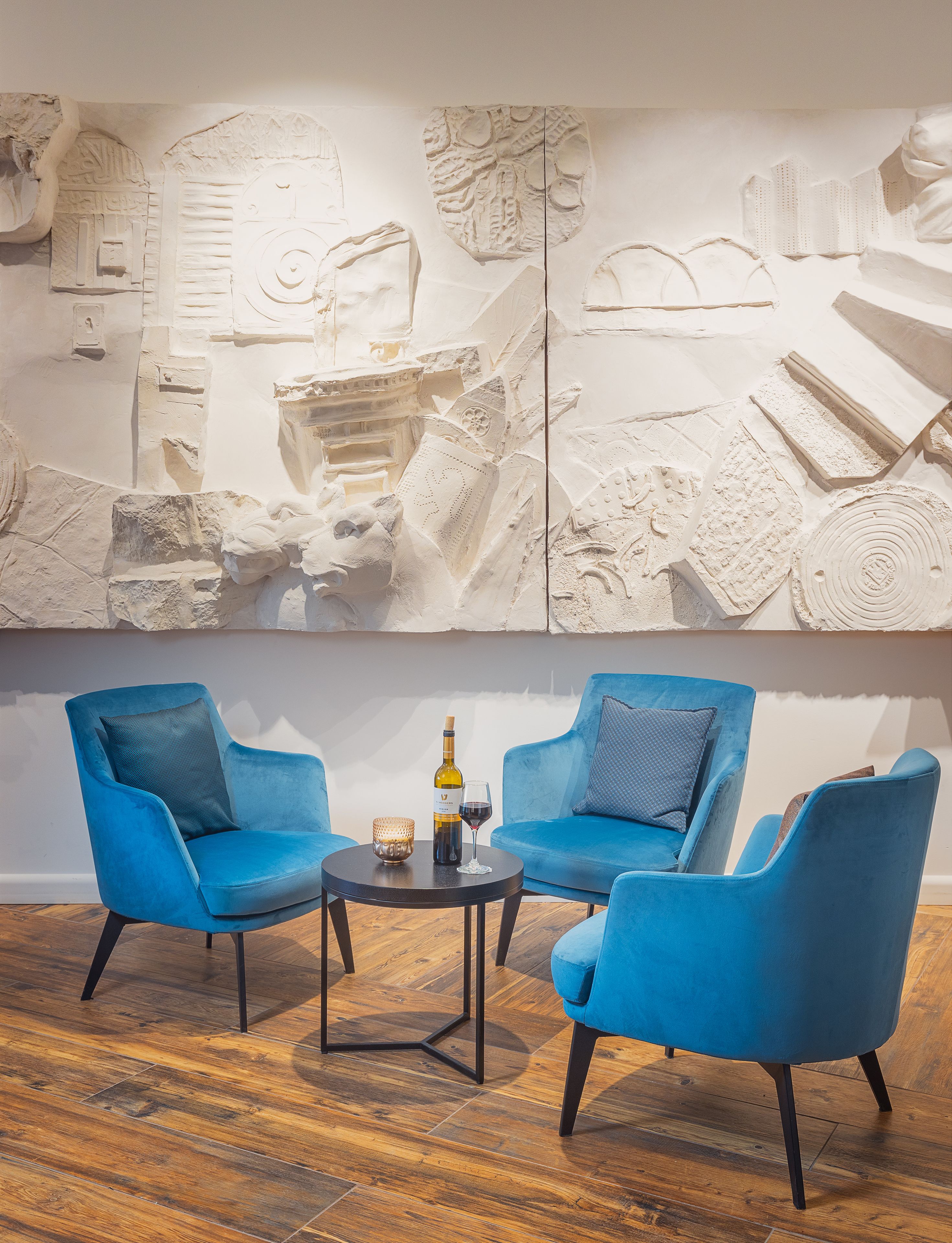 A modern room with two blue armchairs, a small round table, and a decorative wall with intricate carvings.