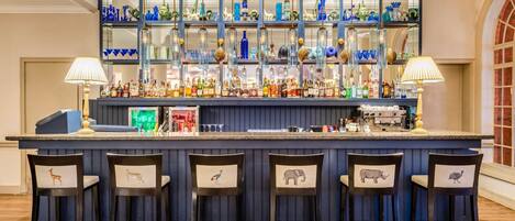 A bar area with a blue bar counter, multiple shelves with glassware, and four chairs with animal designs.