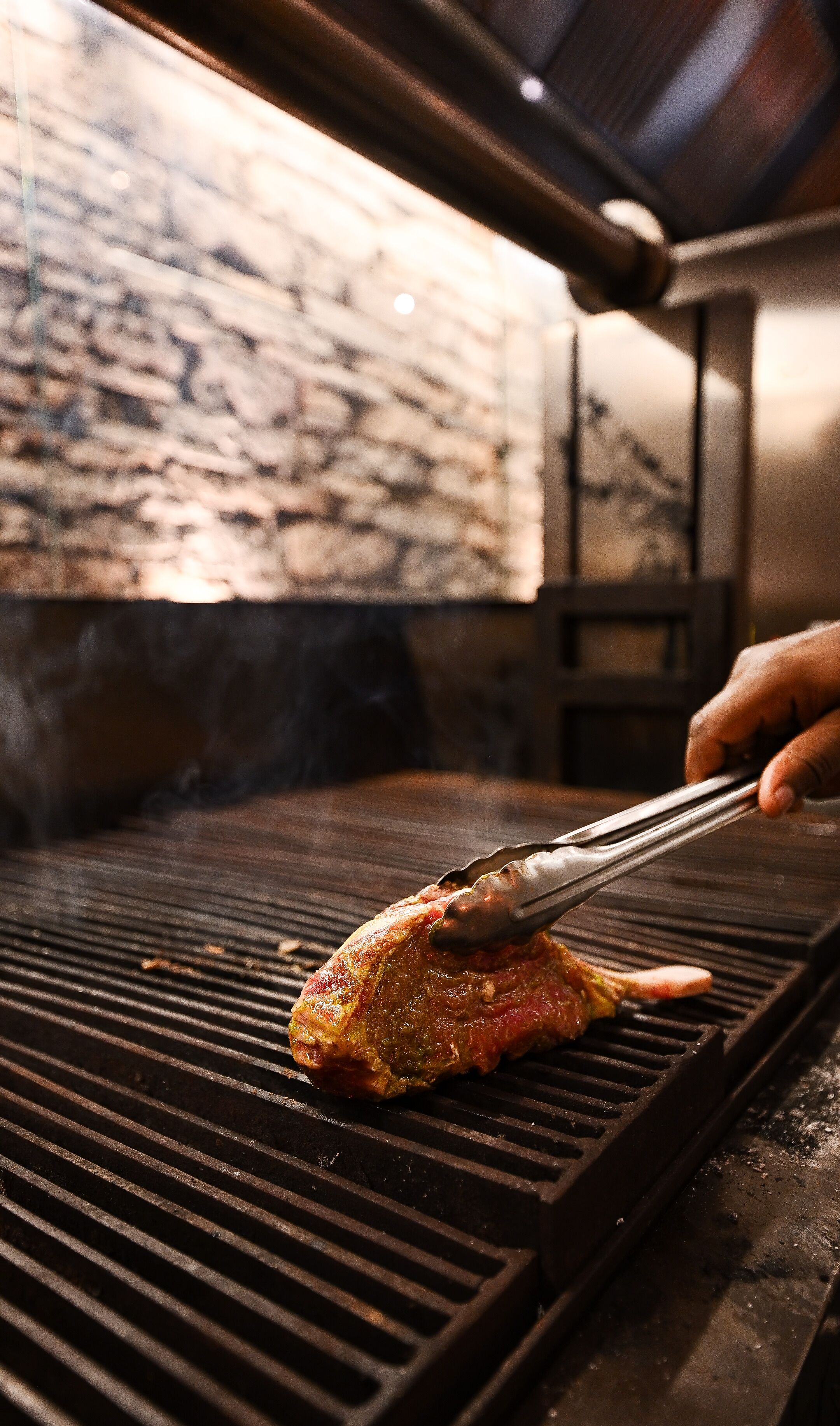 A close-up of a meat being grilled on a grill with a hand using tongs.